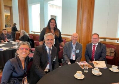 A group of people, including Nick Verginis, CEO of SENVIC, sit around a table, smiling for the camera. A woman stands behind Nick, also smiling.